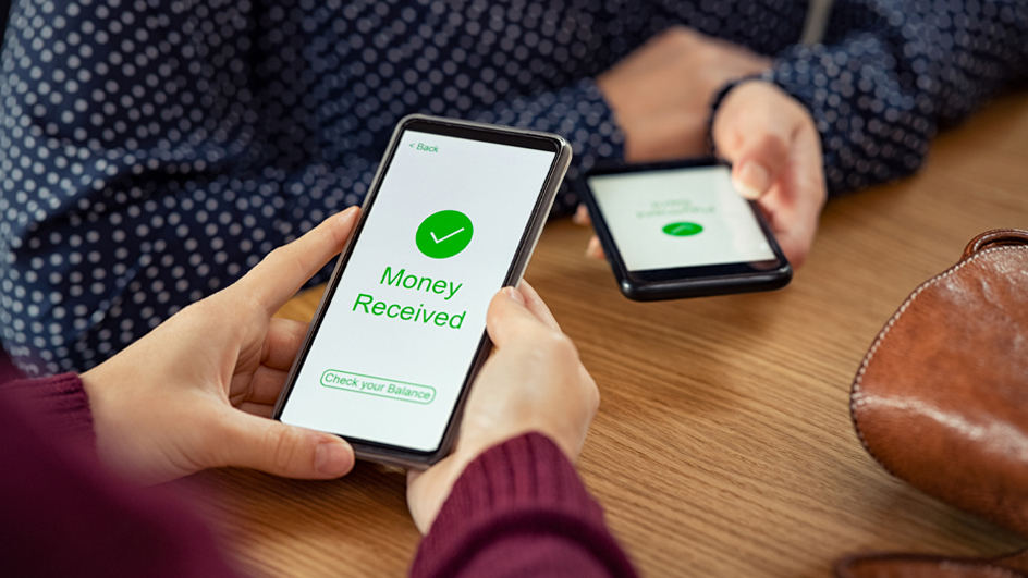 A pair of hands holding a cell phone with the words “money received” in green on the screen