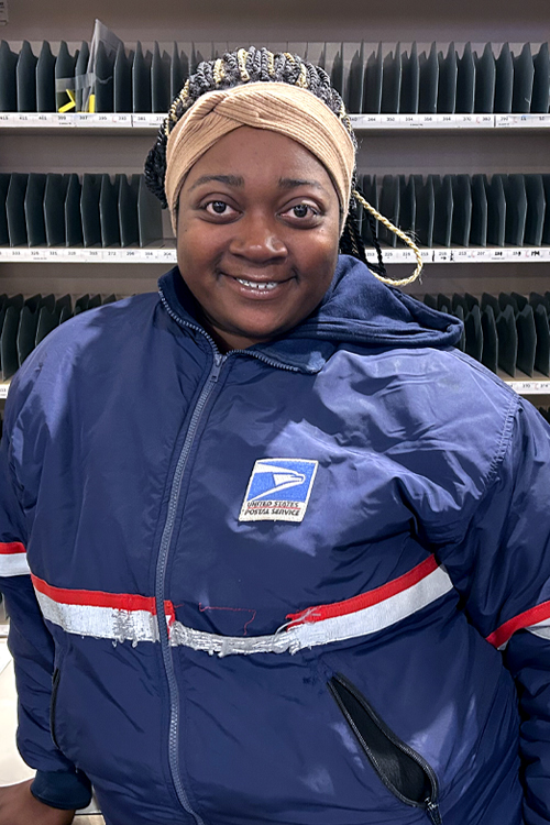 Employee in a USPS jacket standing in front of mail sorting shelves