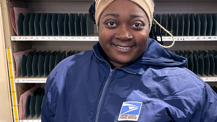 Employee in a USPS jacket standing in front of mail sorting shelves