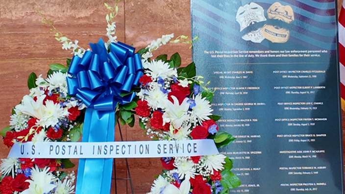 Two postal inspectors standing on either side of a memorial wreath of flowers in USPS headquarters lobby