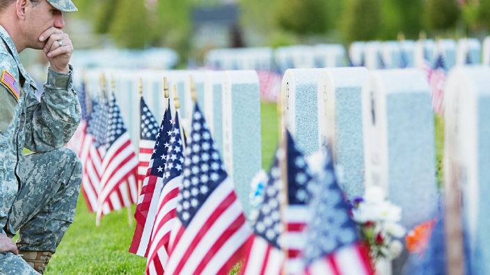 A uniformed American soldier kneeling beside graves decorated with American flags