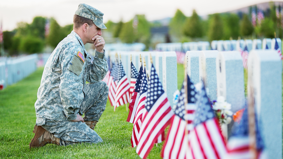 A uniformed American soldier kneeling beside graves decorated with American flags