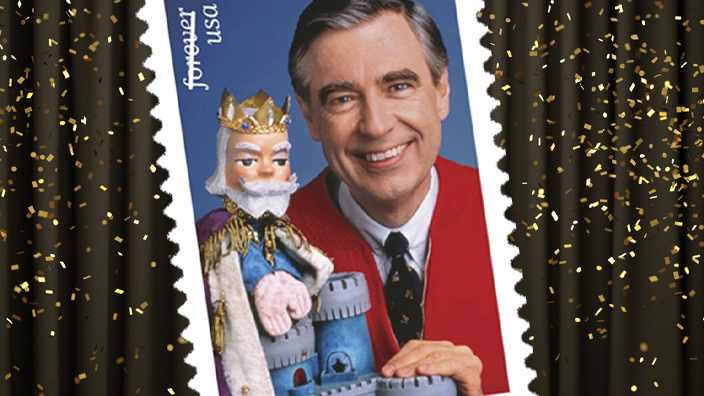An image of the 2018 USPS Mister Rogers stamp showing a man wearing a red button-up sweater and tie, along with a wooden puppet of a king character.