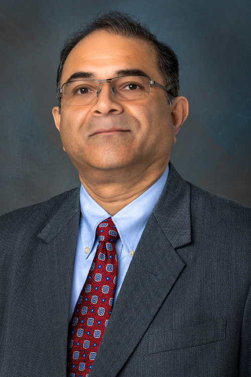 Studio portrait of a smiling man wearing a gray suit with a red tie