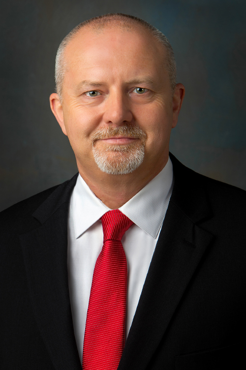 Studio portrait of a smiling man wearing a dark suit with a red tie