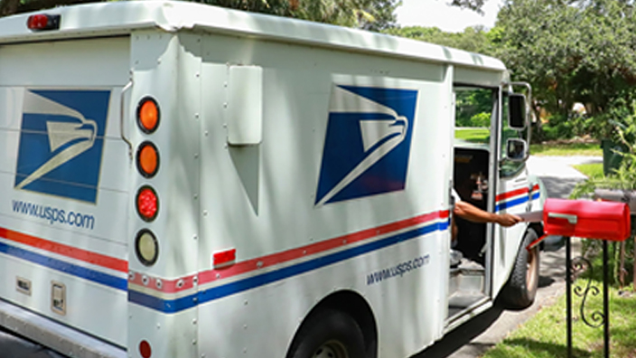 An arm reaches out of USPS delivery vehicle to place letters into a red mailbox