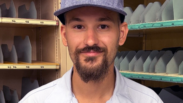 USPS employee wearing a light blue button-up shirt and a blue hat