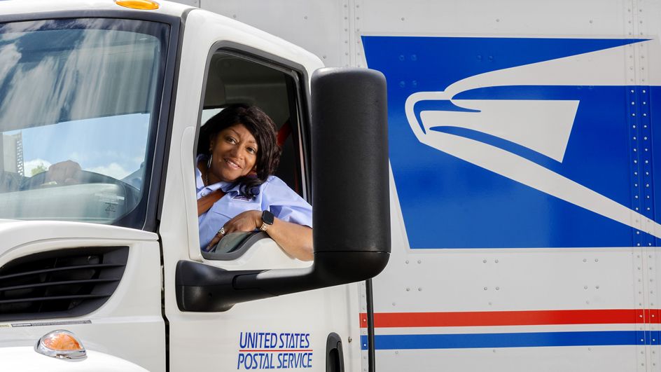 A female employee wearing a seat belt while driving a USPS tractor-trailer