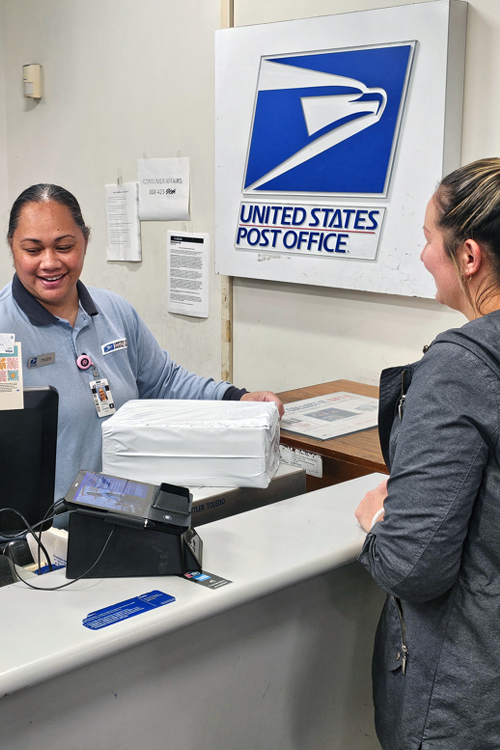 USPS employee behind a Post Office retail counter assisting a customer