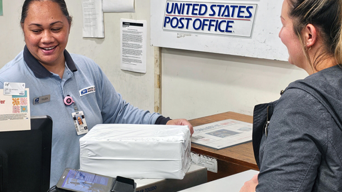 USPS employee behind a Post Office retail counter assisting a customer
