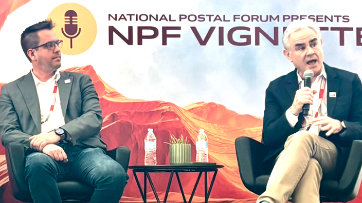 Three people sit side by side on a stage in front a desert-themed backdrop for a panel discussion