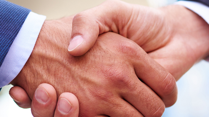 Close-up of a handshake between two people wearing suits