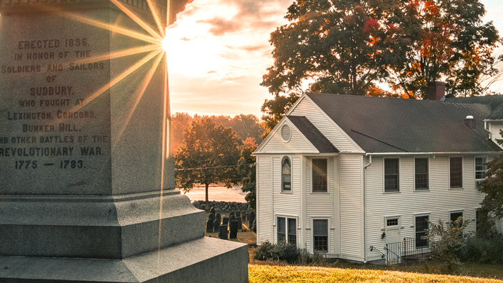 Statue of a soldier positioned on a grassy hill overlooking a church and cemetery