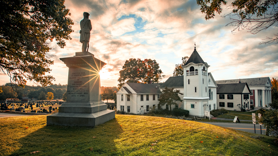Statue of a soldier positioned on a grassy hill overlooking a church and cemetery