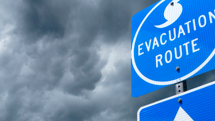 A blue sign indicating the direction of a storm evacuation route against a backdrop of storm clouds