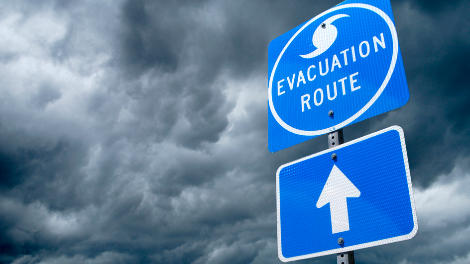 A blue sign indicating the direction of a storm evacuation route against a backdrop of storm clouds