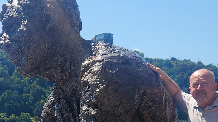 Man standing to the right of a statue of Fred Rogers on a city waterfront