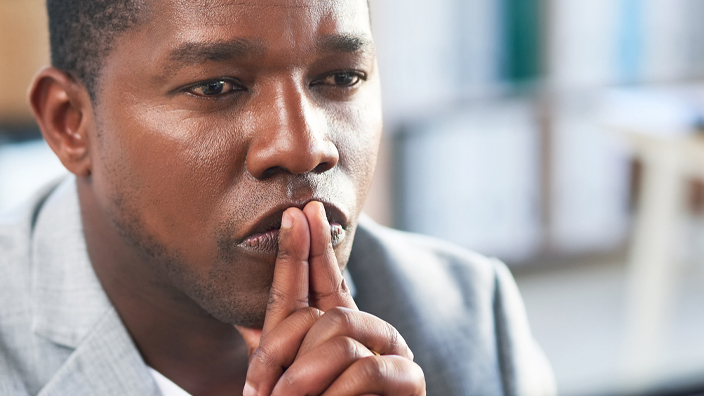 A man with a contemplative expression sits at a desk.