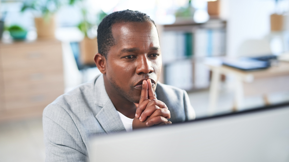 A man with a contemplative expression sits at a desk.