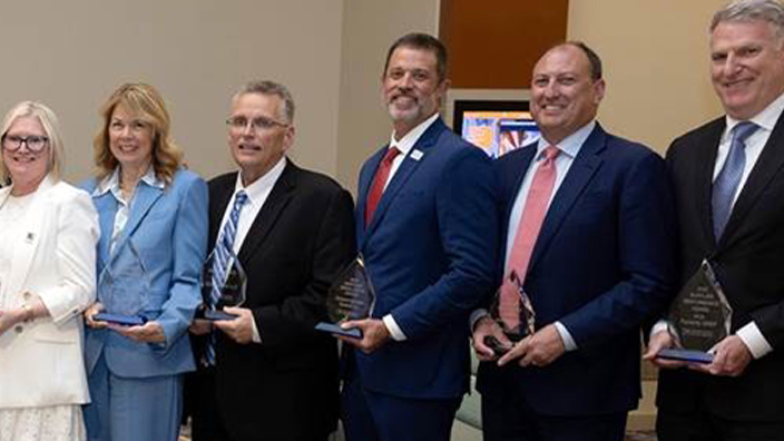 Fourteen people standing together and holding trophies