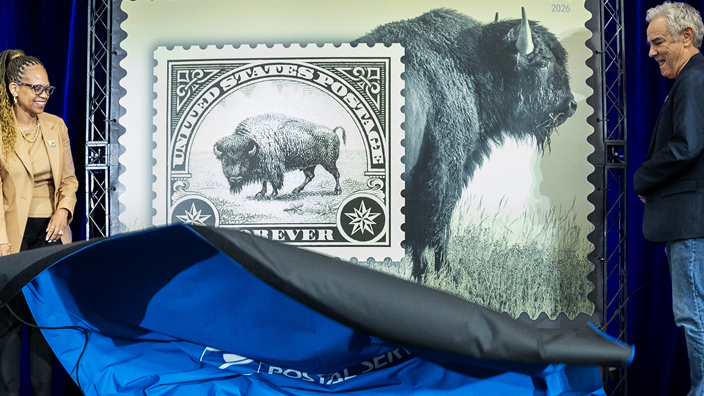 Two groups of three people standing on a stage and on either side of an enlarged image of the American Bison stamp