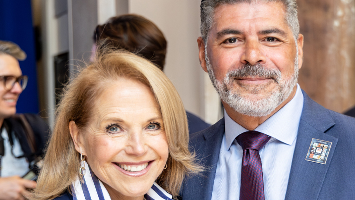 A woman in a dark blue jacket and blue-and-white striped shirt standing next to a man in a blue suit and red tie