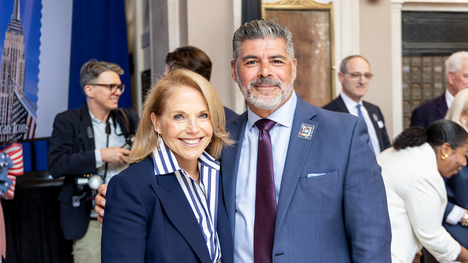A woman in a dark blue jacket and blue-and-white striped shirt standing next to a man in a blue suit and red tie