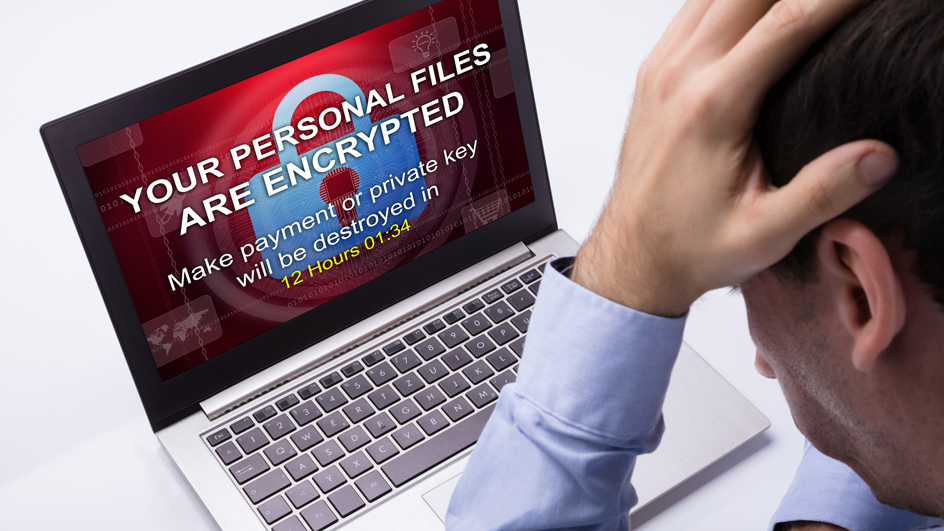 A person staring down at a laptop screen displaying a ransomware message