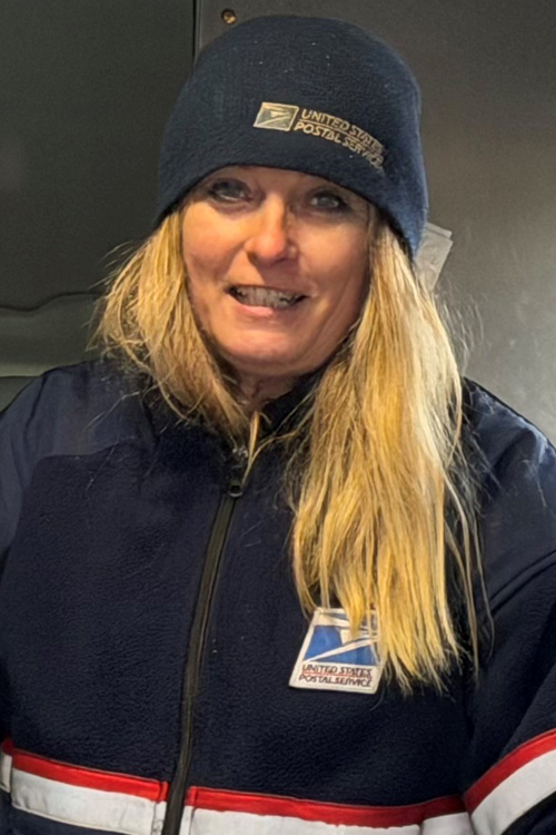 Postal worker in a USPS jacket standing inside a mail vehicle