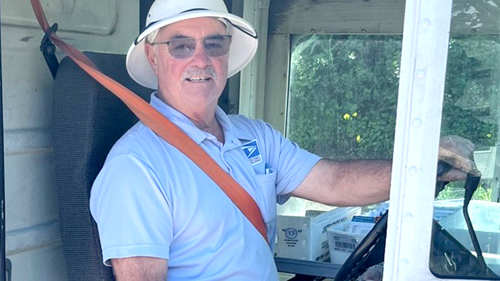 SPS employee wearing a blue uniform and light-colored hat and sitting in driver’s seat of a delivery vehicle with seat belt buckled