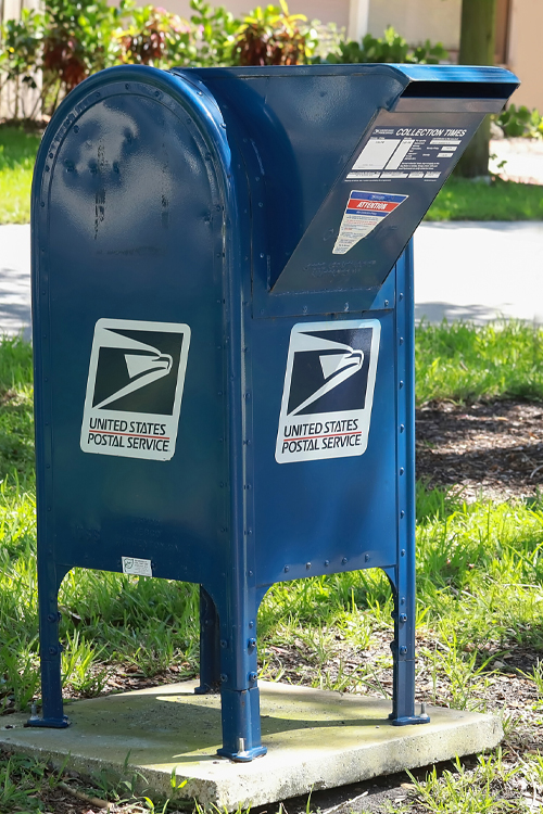 Blue USPS mail collection box bolted to a concrete pad outdoors