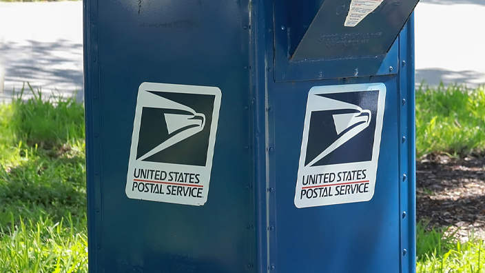 Blue USPS mail collection box bolted to a concrete pad outdoors