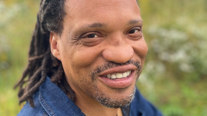 Smiling man wearing denim and crouching in a field