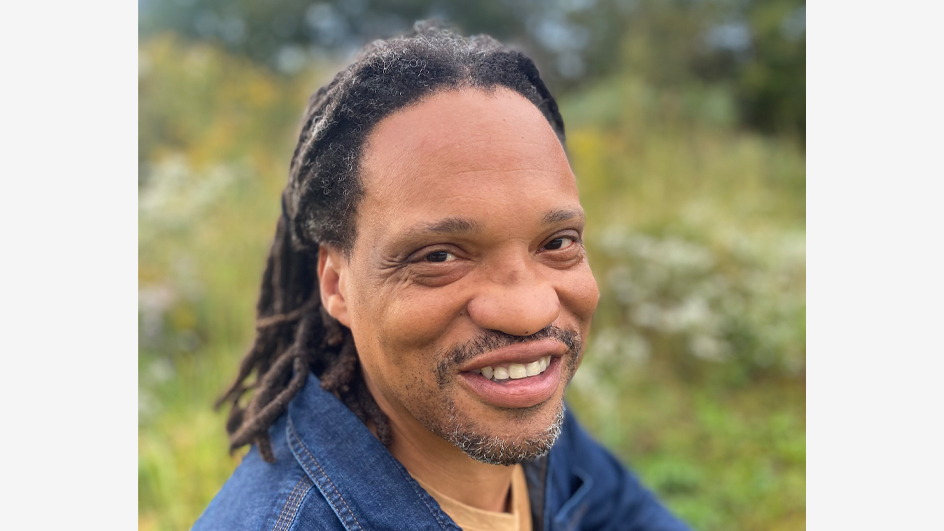 Smiling man wearing denim and crouching in a field