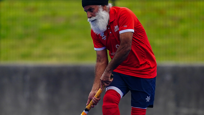 Man in red shirt, blue shorts and red socks playing field hockey