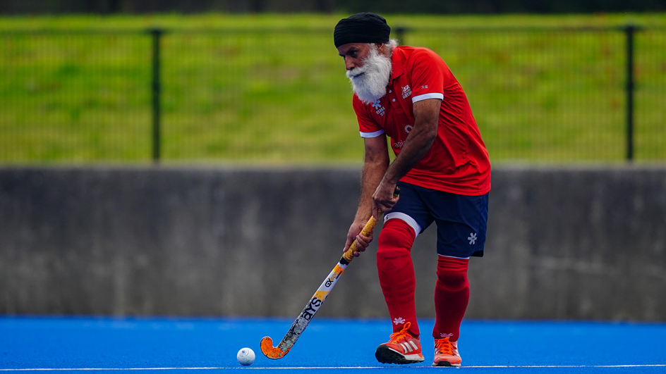 Man in red shirt, blue shorts and red socks playing field hockey