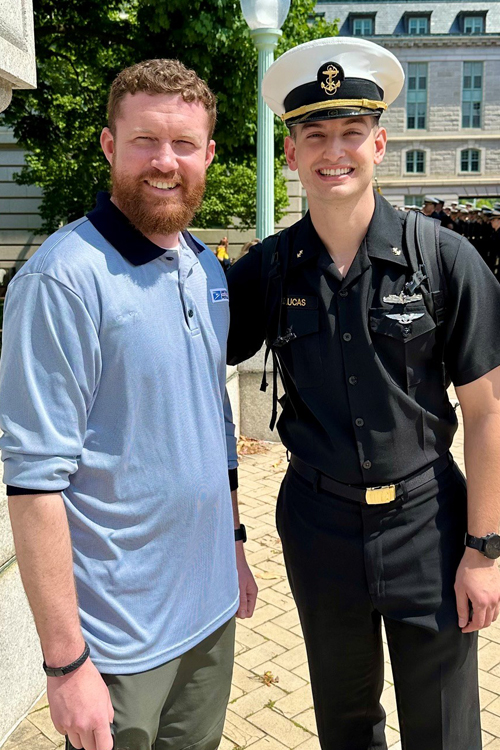 USPS employee in a blue polo shirt standing next to a U.S. Naval Academy midshipman in a black military uniform