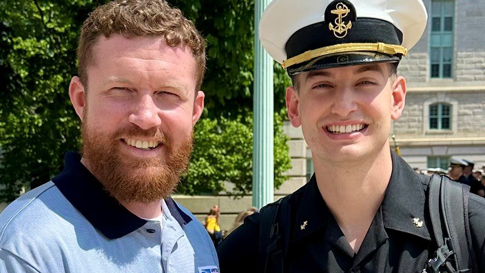 USPS employee in a blue polo shirt standing next to a U.S. Naval Academy midshipman in a black military uniform