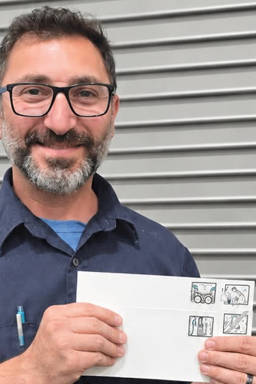 USPS employee in a blue button-up shirt holding up drawings of a drum set, microphone, and two guitars on Advanced Facer Canceler System test cards