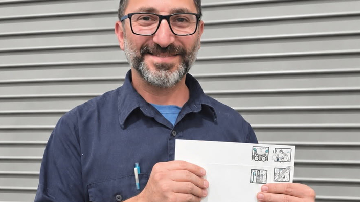 USPS employee in a blue button-up shirt holding up drawings of a drum set, microphone, and two guitars on Advanced Facer Canceler System test cards