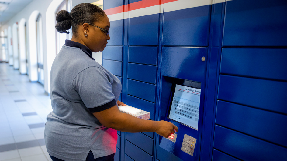 A USPS employee uses the screen on a bank of blue package lockers.