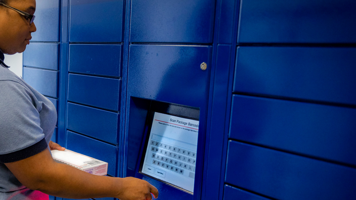 A USPS employee uses the screen on a bank of blue package lockers.
