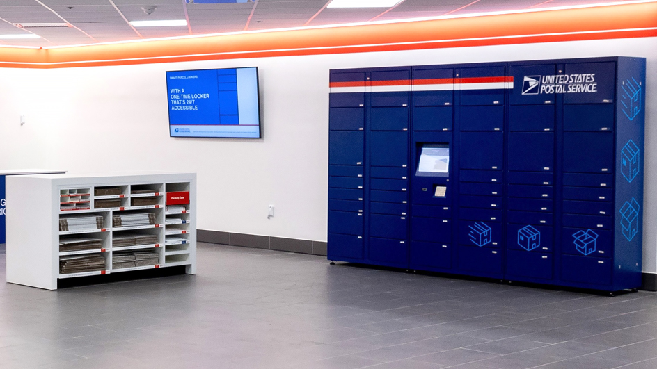A bank of blue package lockers inside a Post Office lobby.
