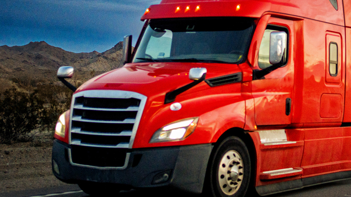 Red semi-truck speeding on a two-lane highway with cars in background