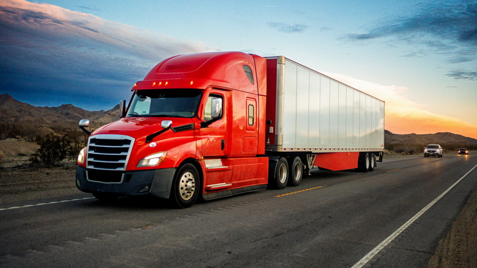Red semi-truck speeding on a two-lane highway with cars in background