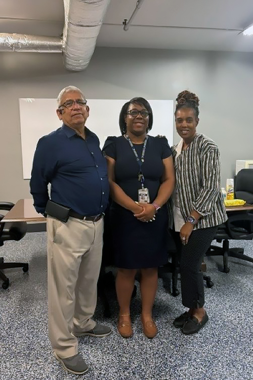 Three professionally dressed people standing side by side in an office conference room