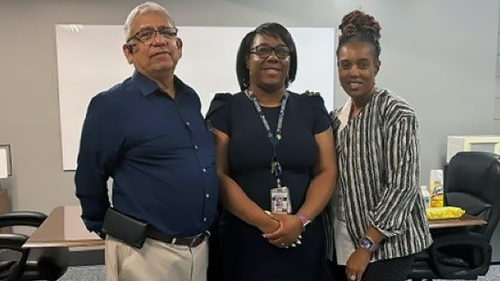 Three professionally dressed people standing side by side in an office conference room