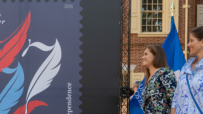 Three ceremony participants stand on each side of an enlarged image of the Declaration of Independence stamp