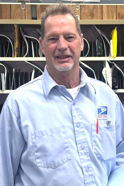 USPS employee in uniform standing in front of a mail sorting station