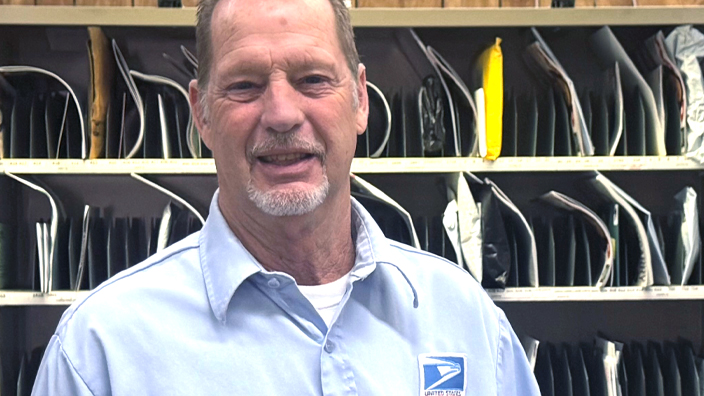 USPS employee in uniform standing in front of a mail sorting station